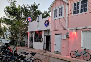 Saloon 1, a Key West gay bar in Florida. The bar's entrance is visible, with bikes parked nearby. Pink building next door.