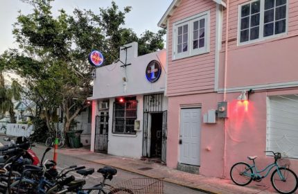 Saloon 1, a Key West gay bar in Florida. The bar's entrance is visible, with bikes parked nearby. Pink building next door.