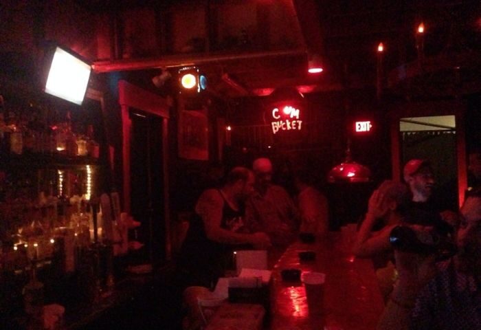 Saloon 1 Key West gay bar in Florida. Red lighting, bar with patrons, and a neon sign that reads C*m Bucket. Nightlife scene.