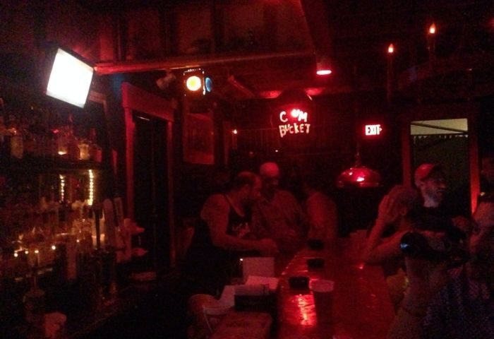 Saloon 1 Key West gay bar in Florida. Red lighting, bar with patrons, and a neon sign that reads C*m Bucket. Nightlife scene.