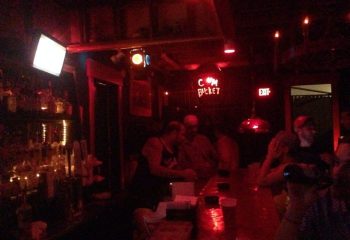 Saloon 1 Key West gay bar in Florida. Red lighting, bar with patrons, and a neon sign that reads C*m Bucket. Nightlife scene.