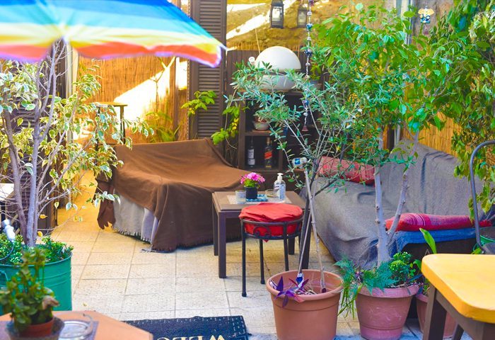 Cozy outdoor seating at Sami's Bar, Athens. Lush greenery, colorful umbrella, and relaxed atmosphere. Gay travel guide recommendation.