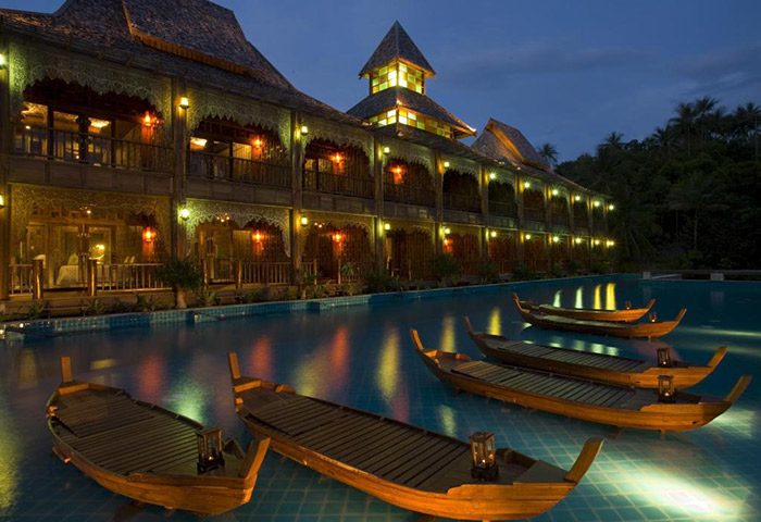 Santhiya Koh Phangan Resort & Spa pool villas at night. Luxury gay travel destination with illuminated wooden boats in the pool.