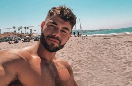 Sasha Bloom by Sasha: Gay travel influencer shirtless on beach. Outdoor photo of handsome, bearded man. Gay travel advice, beach vacation.