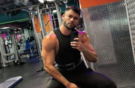 Sasha Bloom by Sasha: Muscular gay man takes a selfie at the gym. He's wearing a black tank top and pants. Gay travel advice.