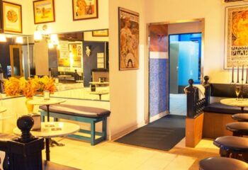 Interior of Sauna Bruc, a gay sauna in Barcelona. Seating area with benches, tables, and bar stools. Art Deco posters on the walls.