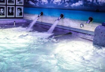 Sauna Bruc's jacuzzi in Barcelona. Water pours from spouts into the pool. A beach scene mural adorns the wall. Gay sauna travel advice.