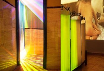 Sauna Bruc: Barcelona gay sauna interior. Rainbow light in showers, green privacy screens, and a suggestive image on the wall.