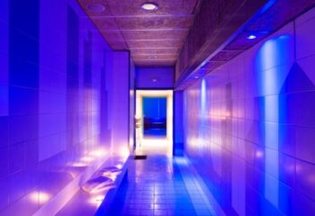 Hallway at Casanova, a gay sauna in Barcelona. Blue lighting, tiled walls, and towels on a bench. Gay travel and nightlife destination.