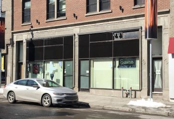 Montreal's Sauna Centre-Ville, a gay cruising spot. Building exterior with large windows and a parked car. Urban scene, gay travel.