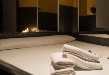 Bedroom at Sauna Condal, a gay sauna in Barcelona. White sheets, towels, and pillows on the bed. Candles provide ambient lighting.