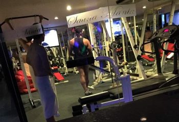 Sauna Mania gay sauna in Bangkok, Silom. Men in towels, gym equipment, and TV screens visible. Gay travel advice for Bangkok's sauna scene.