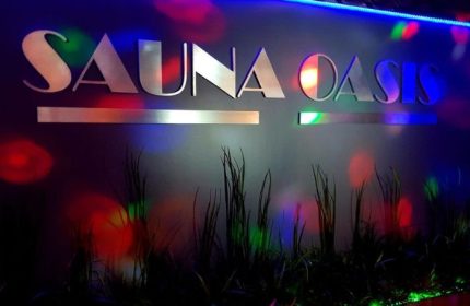 Sauna Oasis in Montreal: Signage with colorful lighting and plants. Gay sauna travel advice for men seeking relaxation and social experiences.