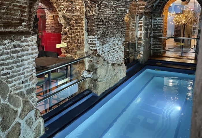 Gay sauna in Madrid's Paraiso Sauna: A pool is surrounded by stone walls. A bar area is visible through an archway. Gay travel.