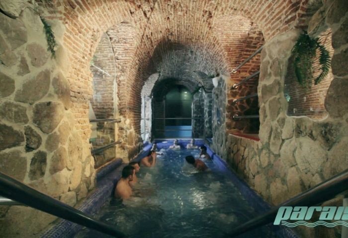 Madrid's Paraiso Gay Sauna: Men relax in a unique stone and brick arched pool area. A gay travel hotspot for relaxation and socializing.