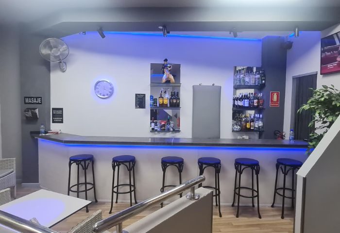 Bar area at a gay sauna in Gran Canaria, Portugal. Blue lights illuminate the bar with stools, shelves of drinks, and a seating area.