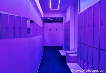 Interior of a gay sauna in Sitges. Lockers and benches line a hallway with purple lighting. Gay travel destination in Spain.