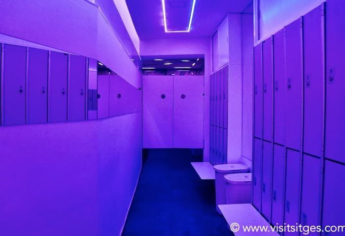Interior of a gay sauna in Sitges. Lockers and benches line a hallway with purple lighting. Gay travel destination in Spain.