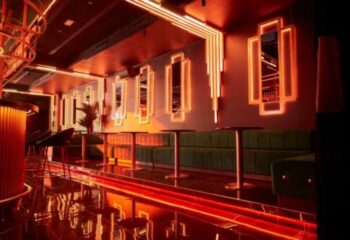 Interior of Thermas Gay Sauna in Barcelona. Art Deco style, red lighting, green velvet seating, bar, tables, mirrors. Gay travel.