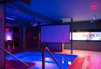 Interior of Thermas Gay Sauna in Barcelona, featuring a small pool with blue lighting, a screen, and a disco ball for gay men's travel.