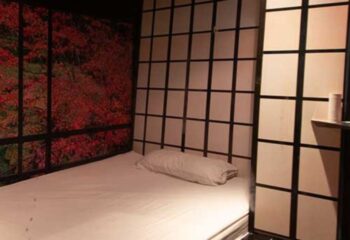 Bedroom at Thermas Gay Sauna in Barcelona. Asian-inspired design with a bed, decorative screen, and a nature-themed mural. Gay travel.