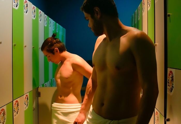 Sauna Beach gay sauna in Madrid: Two shirtless men in towels stand by lockers in the locker room of a gay sauna, Madrid.