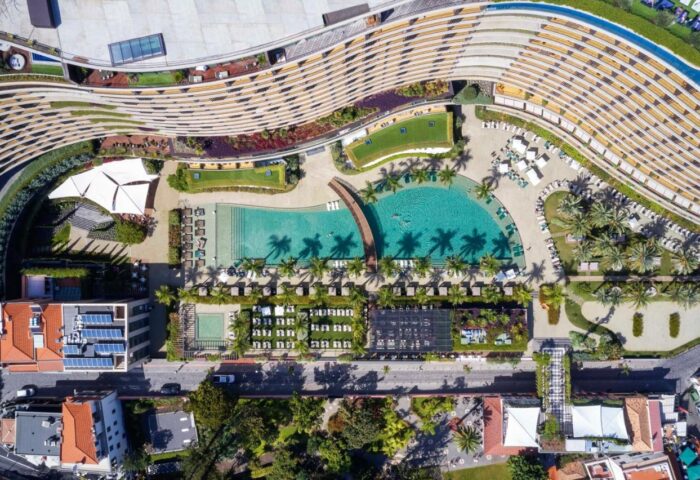 Aerial view of Savoy Palace Madeira, a gay-friendly hotel. Pools, palm trees, and modern architecture offer a luxurious travel experience.