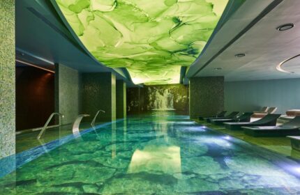 Savoy Palace Madeira pool. Indoor pool with green-toned tile and ceiling art, lounge chairs, and waterfall feature. Gay travel advice.