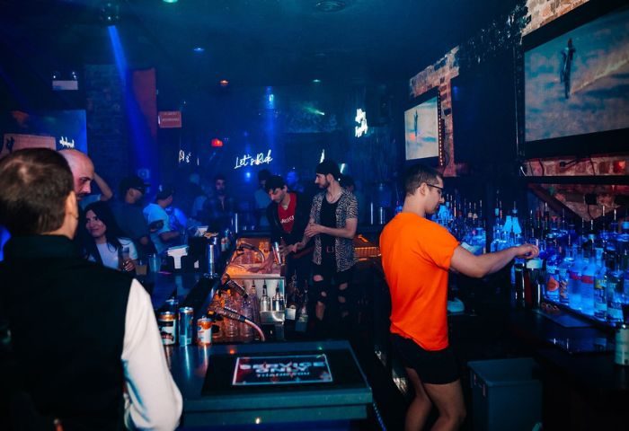 Scarlet Bar, Chicago: Bartender serving drinks at a busy gay party. Blue lighting, neon signs, and diverse crowd. Gay travel advice.