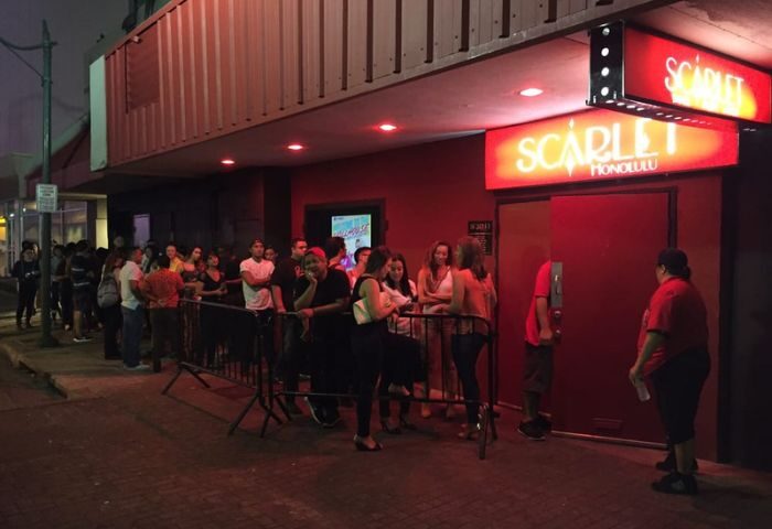 People line up outside Scarlet Honolulu, a gay bar with drag shows. The entrance is red with a bright sign. Gay travel advice.