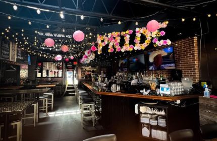Interior of Score on Davie, a Vancouver sports bar. PRIDE in flowers, pink lanterns, bar stools, TVs, and string lights.