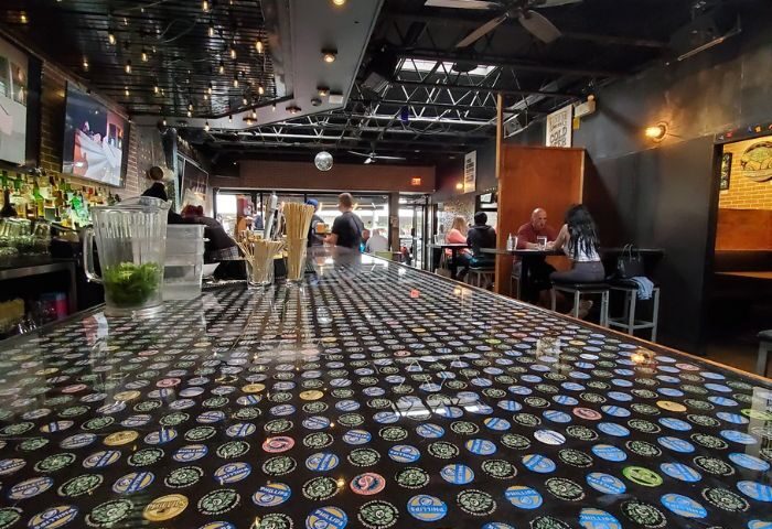 Score on Davie bar interior, Vancouver. Bottle cap-covered bar top, patrons at tables. Gay travel advice, sports & nightlife.