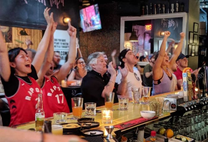 Excited fans at Score on Davie sports bar in Vancouver. People cheering, watching a game, enjoying drinks. Gay-friendly sports bar atmosphere.
