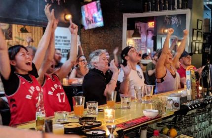 Excited fans at Score on Davie sports bar in Vancouver. People cheering, watching a game, enjoying drinks. Gay-friendly sports bar atmosphere.