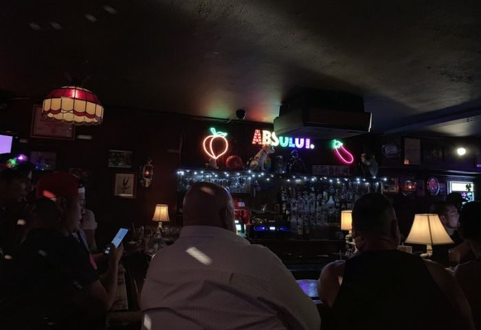 Second Story Bar gay night party in Chicago. People at the bar with neon signs. Gay travel advice for men.