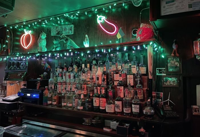 Second Story Bar, a gay bar in Chicago, at night. Bottles line the bar, with neon peach and eggplant signs, and green lights above.