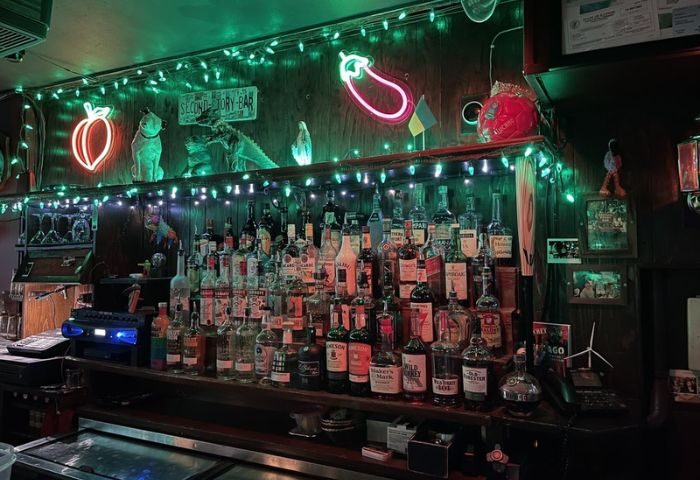 Second Story Bar, a gay bar in Chicago, at night. Bottles line the bar, with neon peach and eggplant signs, and green lights above.
