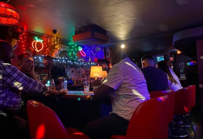 People at a second-story gay bar in Chicago. Neon lights, including a peach and eggplant, decorate the bar during a night party.