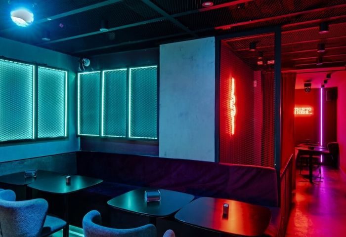 Secret Room Bar, a gay bar in Madrid. Blue and red neon lights illuminate tables and seating. A stylish, modern interior design.