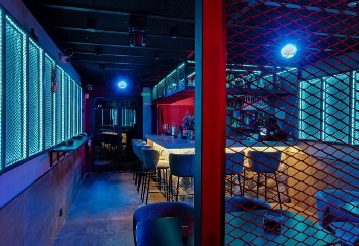 Interior of Secret Room Bar, a gay bar in Madrid. Red and blue neon lighting, bar stools, and a modern, stylish design. Nightlife.