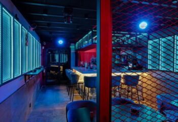 Interior of Secret Room Bar, a gay bar in Madrid. Red and blue neon lighting, bar stools, and a modern, stylish design. Nightlife.