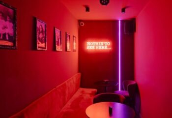 Madrid's Secret Room Bar, a gay bar, features red decor, framed photos, a plush banquette, and a neon sign saying Nothin' to see here.