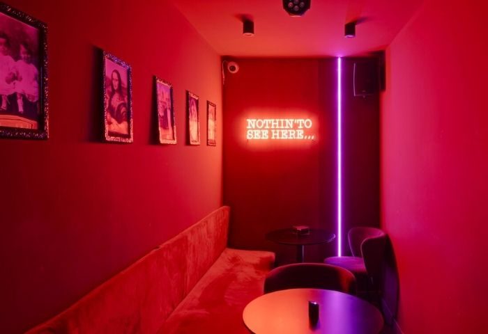 Madrid's Secret Room Bar, a gay bar, features red decor, framed photos, a plush banquette, and a neon sign saying Nothin' to see here.