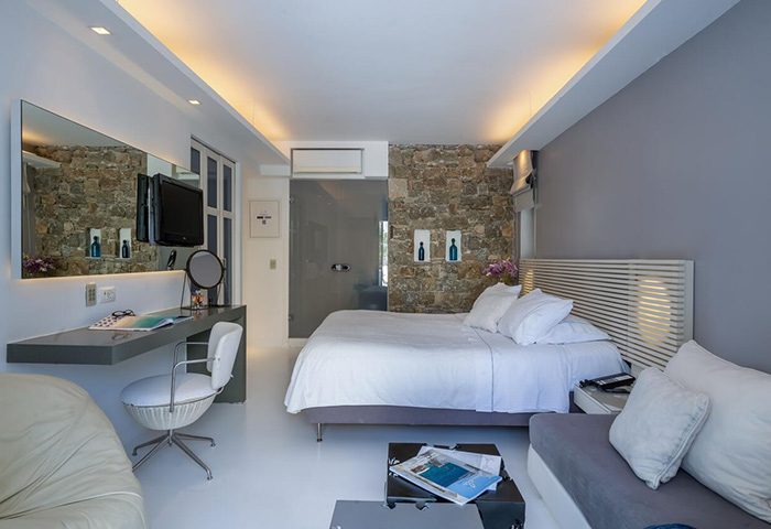 Semeli Hotel Mykonos room. Modern design, white linens, stone wall, desk, and seating area. Popular choice for gay travelers & honeymooners.