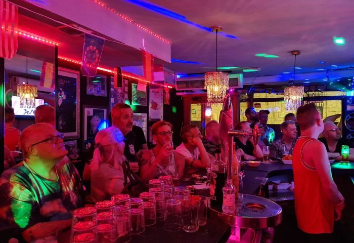 Inside Sensations gay bar in Benidorm, Spain. People at the bar, glasses, bottles, colorful lights. Gay travel destination, nightlife.