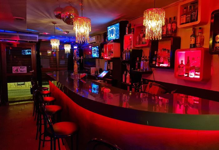 Sensations Gay Bar in Benidorm. Interior view of bar with red lighting, disco balls, chandeliers, bottles, and bar stools. Nightlife.