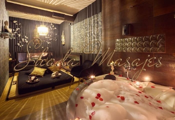 Shada Masajes, a gay massage in Barcelona. Bathtub with bubbles and rose petals. Massage bed with pillows and towels. Relaxing spa.
