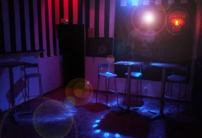 Interior of Shower Bar, a gay cruise club in Madrid. Tables, chairs, and black-and-white striped walls under blue and red lights.