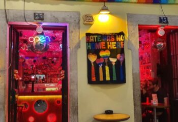 Lisbon gay bar entrance with rainbow flag. Hate Has No Home Here sign. Disco balls, neon lights, and a welcoming atmosphere for LGBTQ+ travelers.