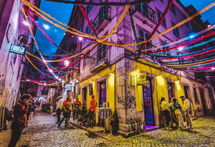 Lisbon's vibrant nightlife: A side-bar in Lisbon, Portugal, glows under colorful streamers. People gather outside, enjoying the gay travel scene.